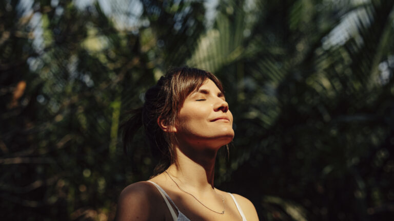 Woman outside in the sunshine with her eyes closed saying a prayer habit