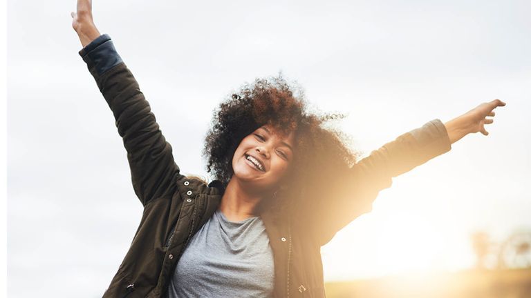 Woman with her arms in the air at sunset after reading devotions on gratitude