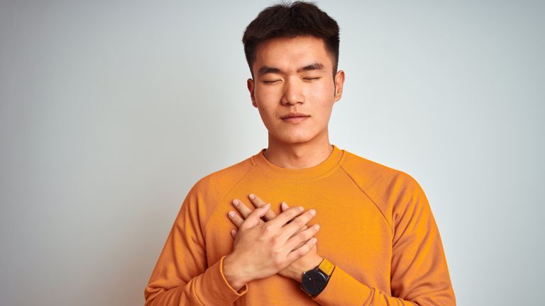 Man in an orange sweater with his hand over his heart asking for forgiveness in the new year