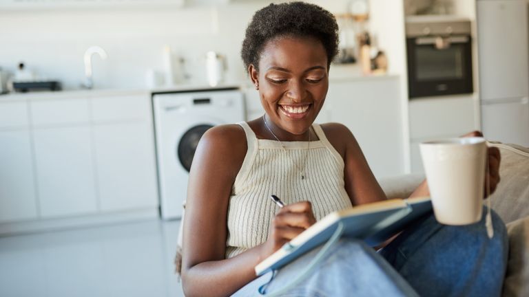 Smiling woman drinking tea writing down her reading habits in a journal