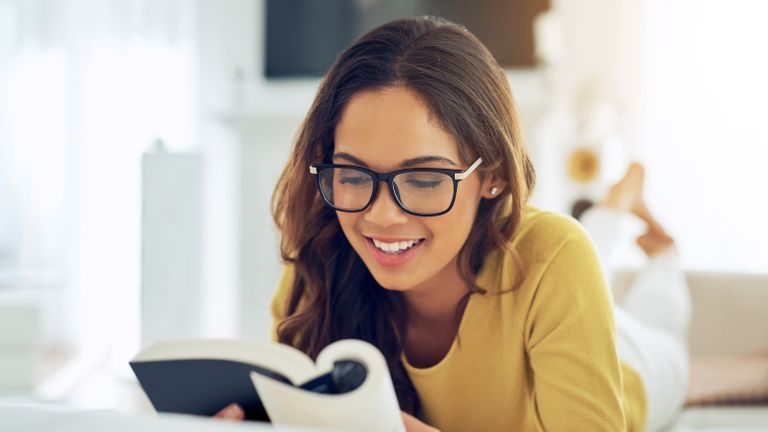 Woman with glasses in yellow shirt does her reading habit in bed