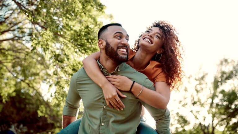 Man giving his girlfriend a piggyback ride outside with quotes about the pursuit of happiness